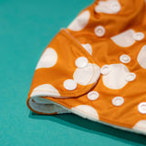 Acercamiento al color y patrón del pañal sostenible Ole ese Poo colocado sobre una superficie de fondo verde