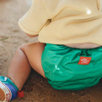 Pañal de tela ecológico greener Poo de color verde llevado por un niño sentado en el suelo