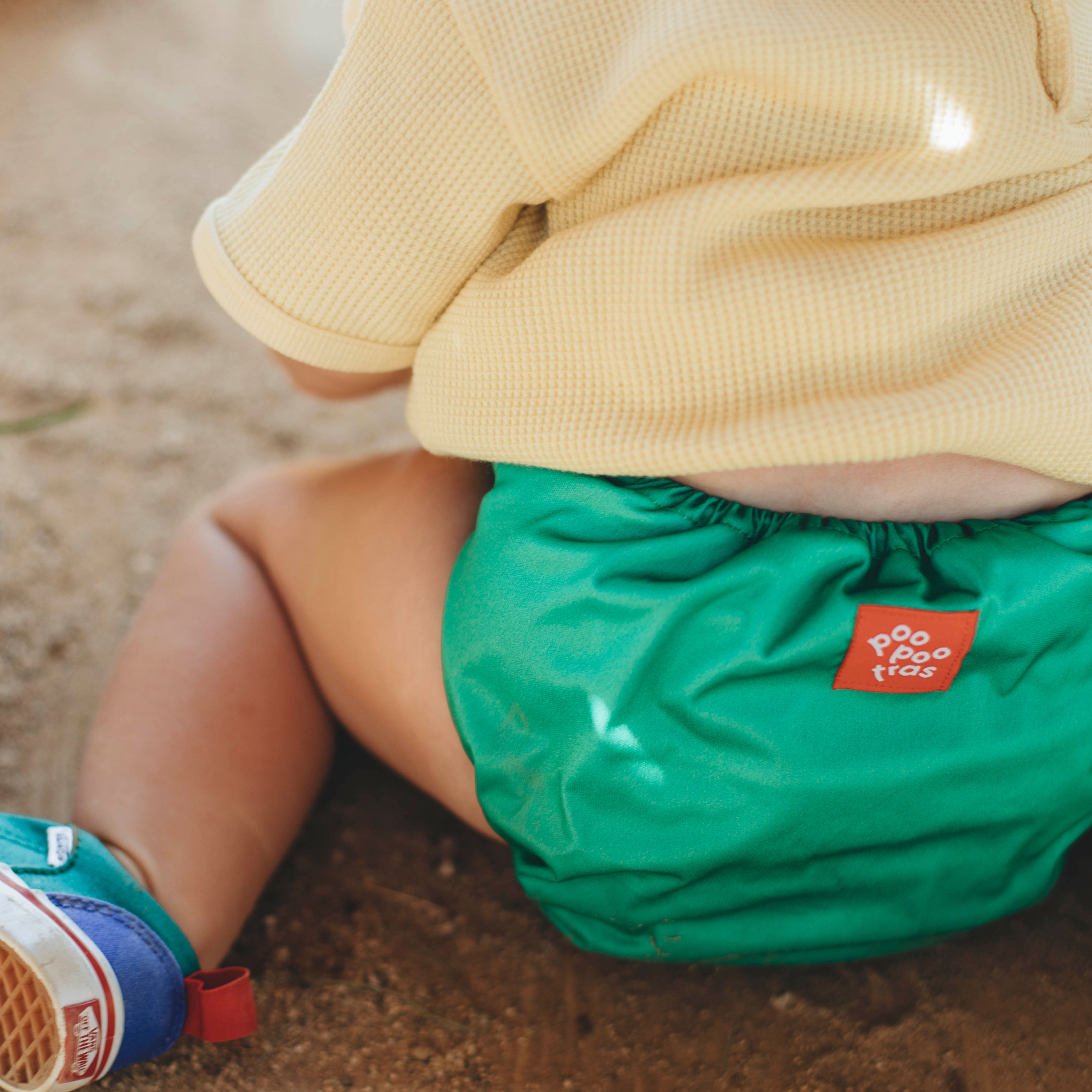 Pañal de tela ecológico greener Poo de color verde llevado por un niño sentado en el suelo